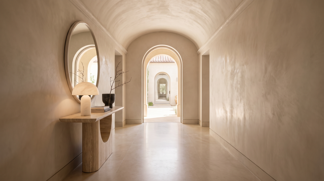 Grand barrel-vaulted hallway with a sculptural travertine console, round mirror and alabaster lamp