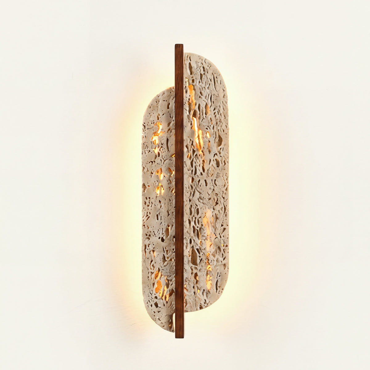 The Foglia travertine wall light, lit on a plaster wall
