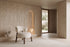 The Bardolino Armchair in off-white boucle beside a fluted travertine wall and lit arched niche