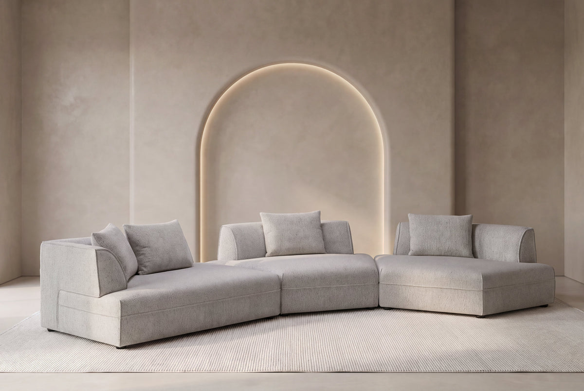The Bergamo Modular Corner Sofa in grey in a tall greige plaster room with an arched niche
