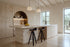 Two Bonassola Counter Stools in black at a travertine kitchen island in a beamed kitchen with olive trees beyond