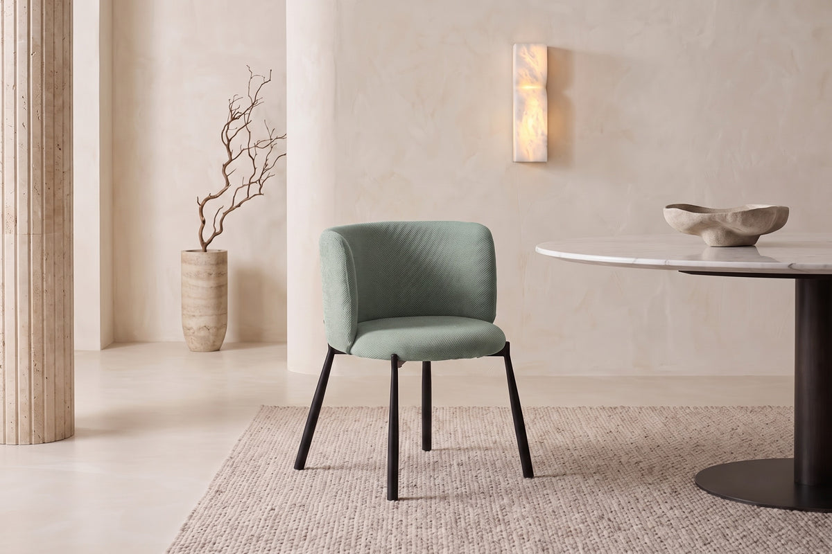 The Bormio Dining Armchair in sage, upholstered dining armchair on black metal legs, styled in a room
