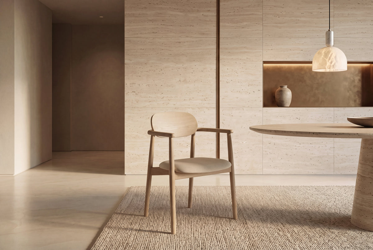 The Brescia Dining Armchair in beige and washed oak beside a travertine dining table beneath an alabaster pendant