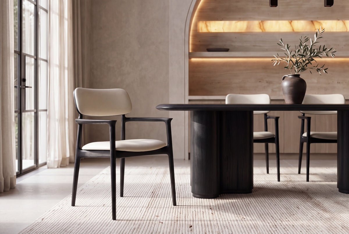 The Brindisi Dining Armchair in black ash and ivory, pulled out from The Brindisi Dining Table in an arched plaster dining room by Kunal Trehan