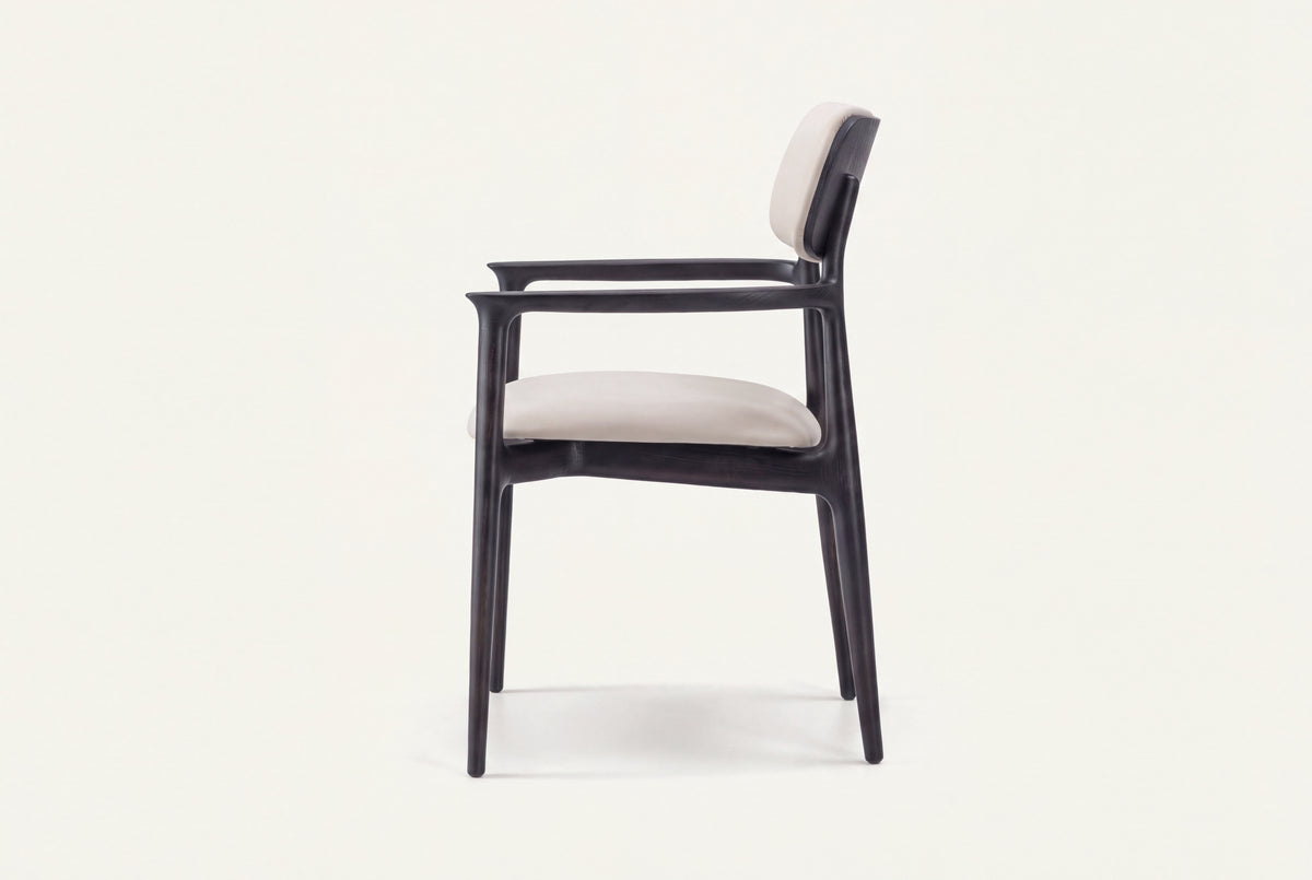 The Brindisi Dining Armchair by Kunal Trehan, side view showing the sculpted black ash frame, open arm and ivory seat