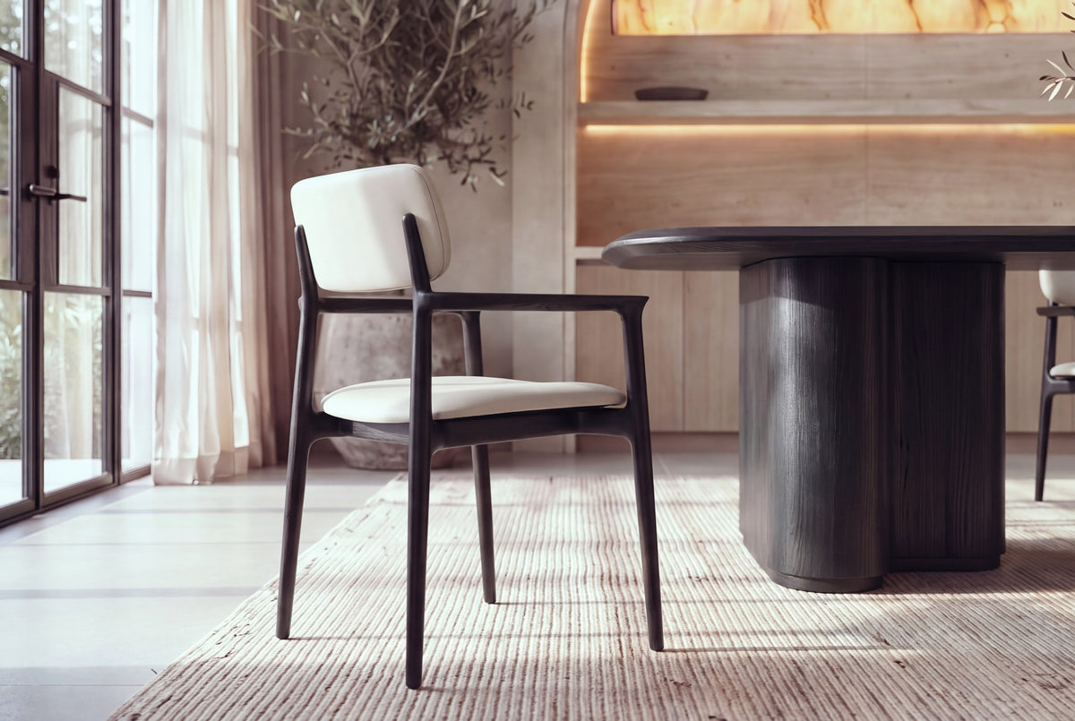 The Brindisi Dining Armchair in black and ivory around The Brindisi Dining Table in a plaster dining room