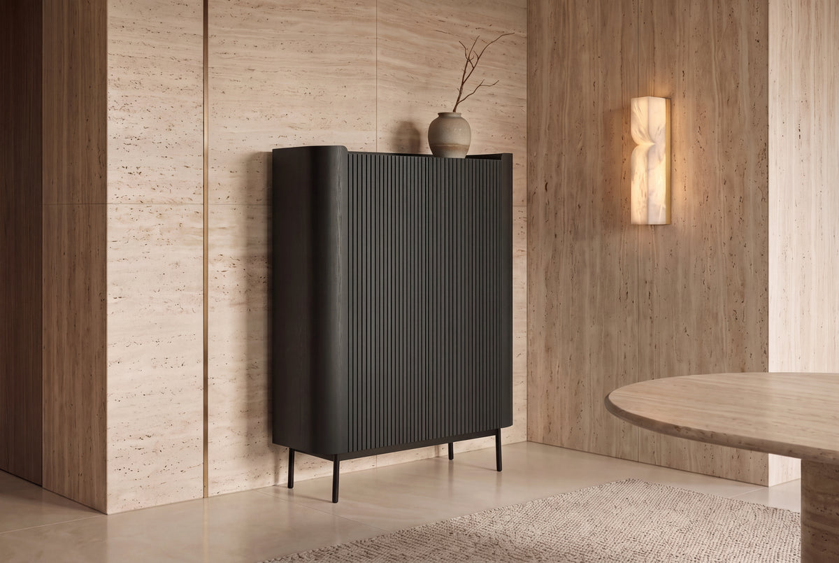 The Camogli Fluted Highboard in black against a travertine wall beside an alabaster wall light