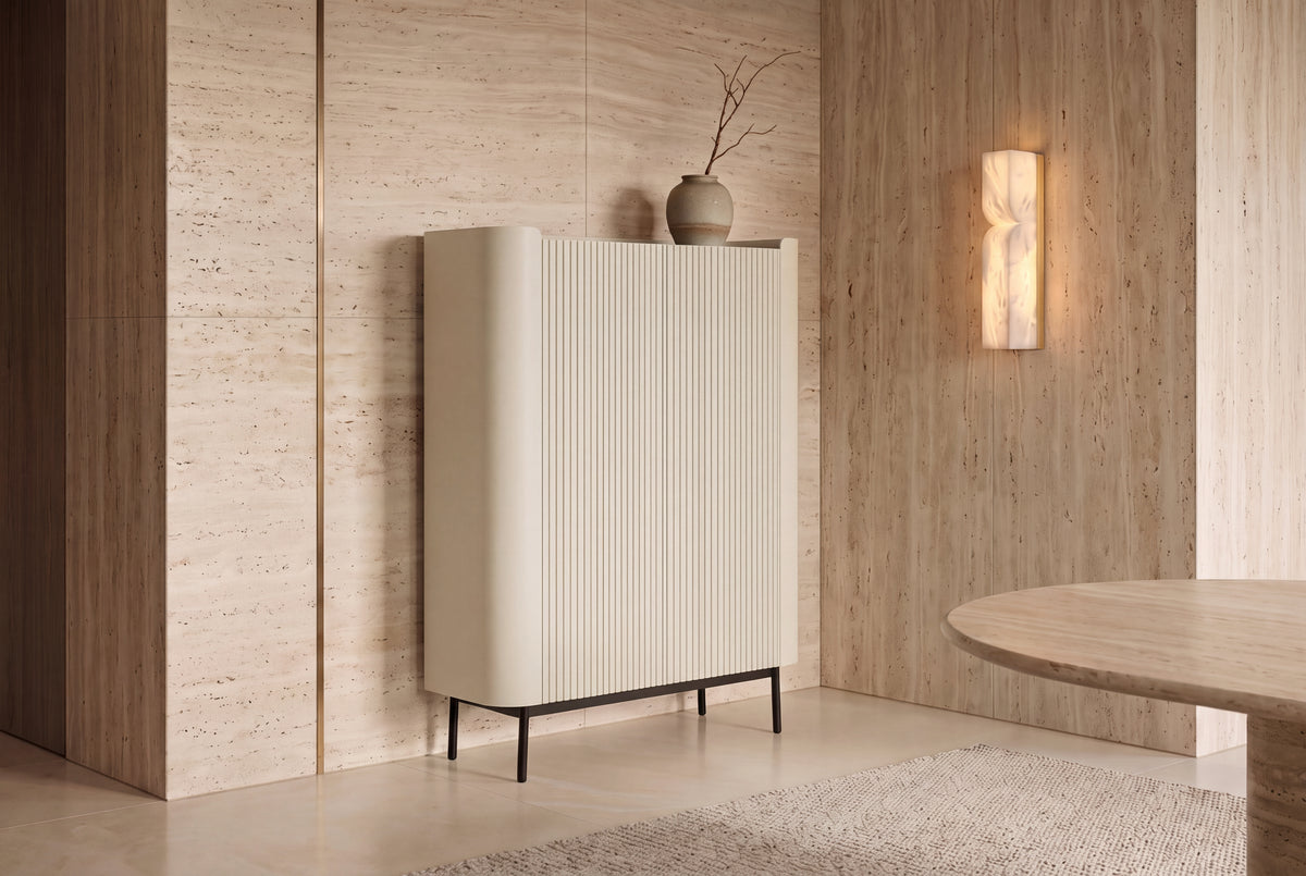 The Camogli Fluted Highboard in cream against a travertine wall beside an alabaster wall light