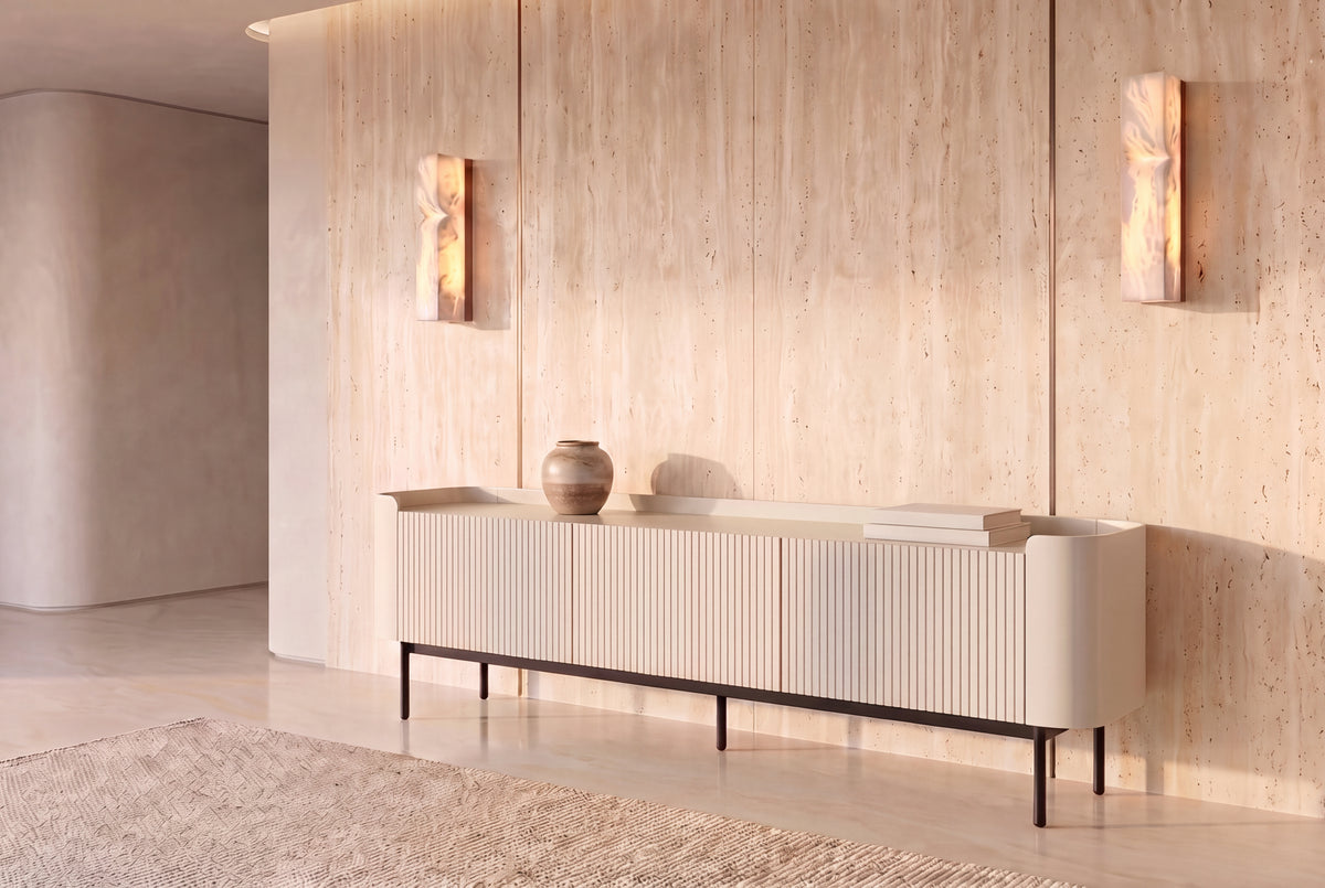 The Camogli Fluted TV Unit in cream against a travertine wall between two alabaster wall lights