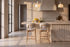 Two Cervo Counter Stools in beige at a fluted travertine kitchen island beneath Cupola alabaster pendants