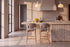 Two Cervo Counter Stools in taupe at a fluted travertine kitchen island beneath Cupola alabaster pendants