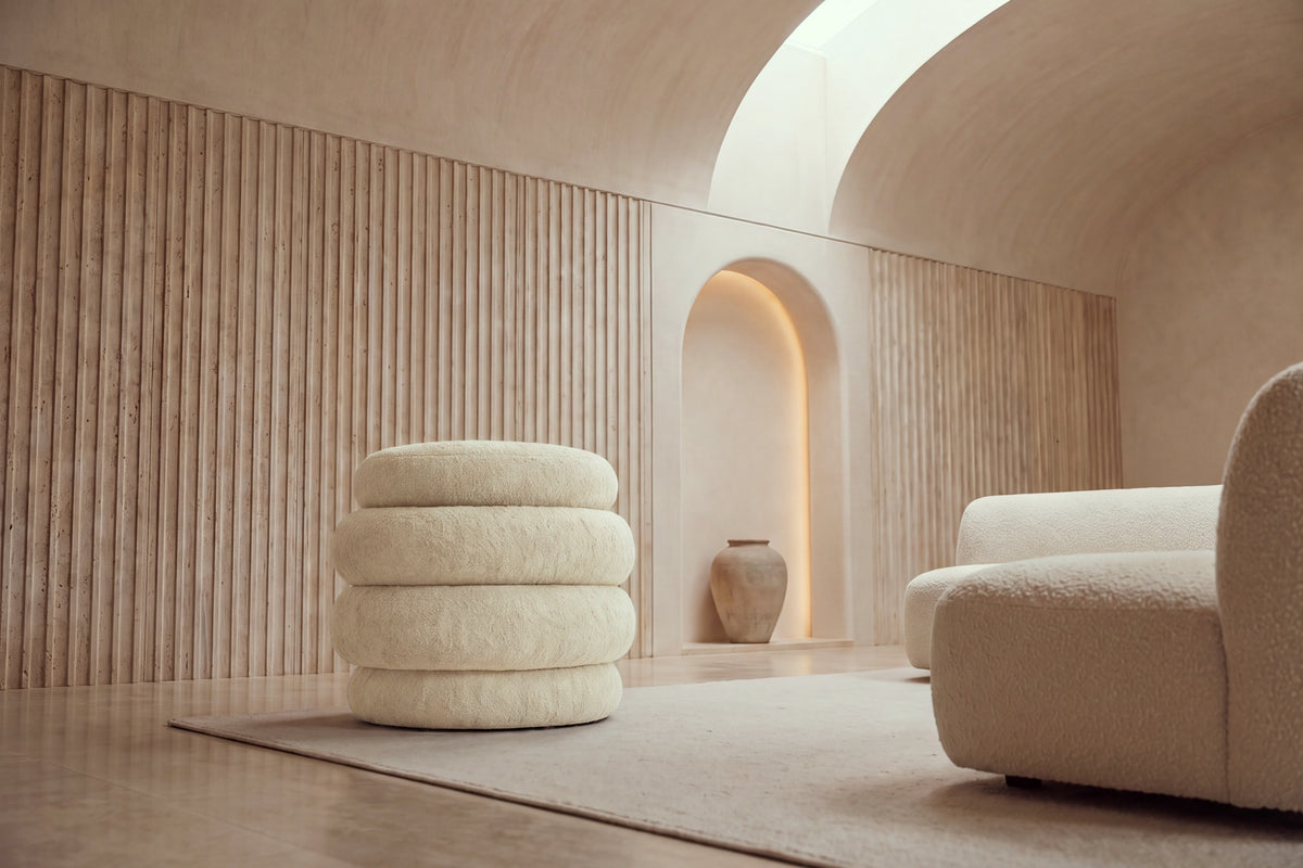The Cisternino pouffe in beige boucle on a wool rug in a vaulted travertine room