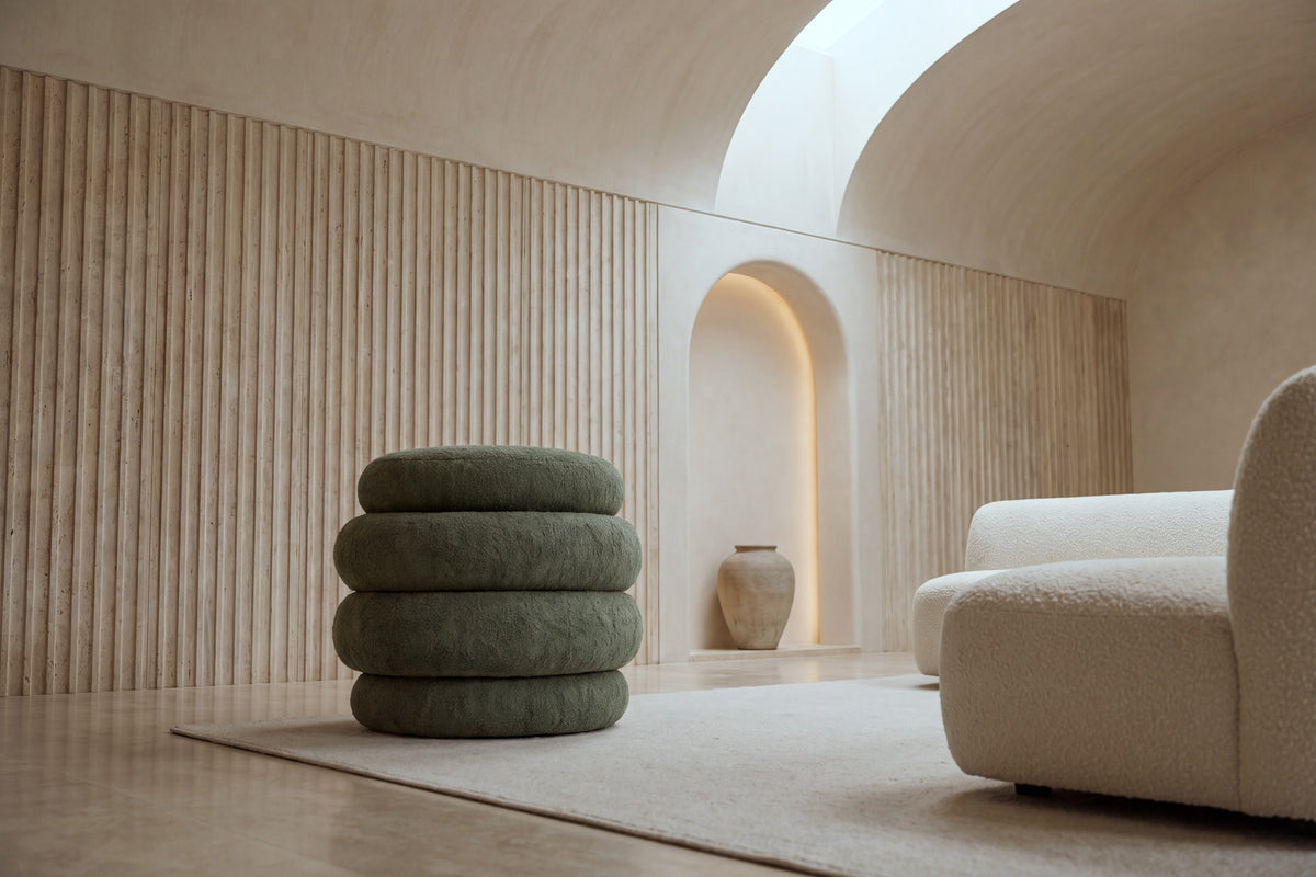 The Cisternino pouffe in green boucle on a wool rug in a vaulted travertine room