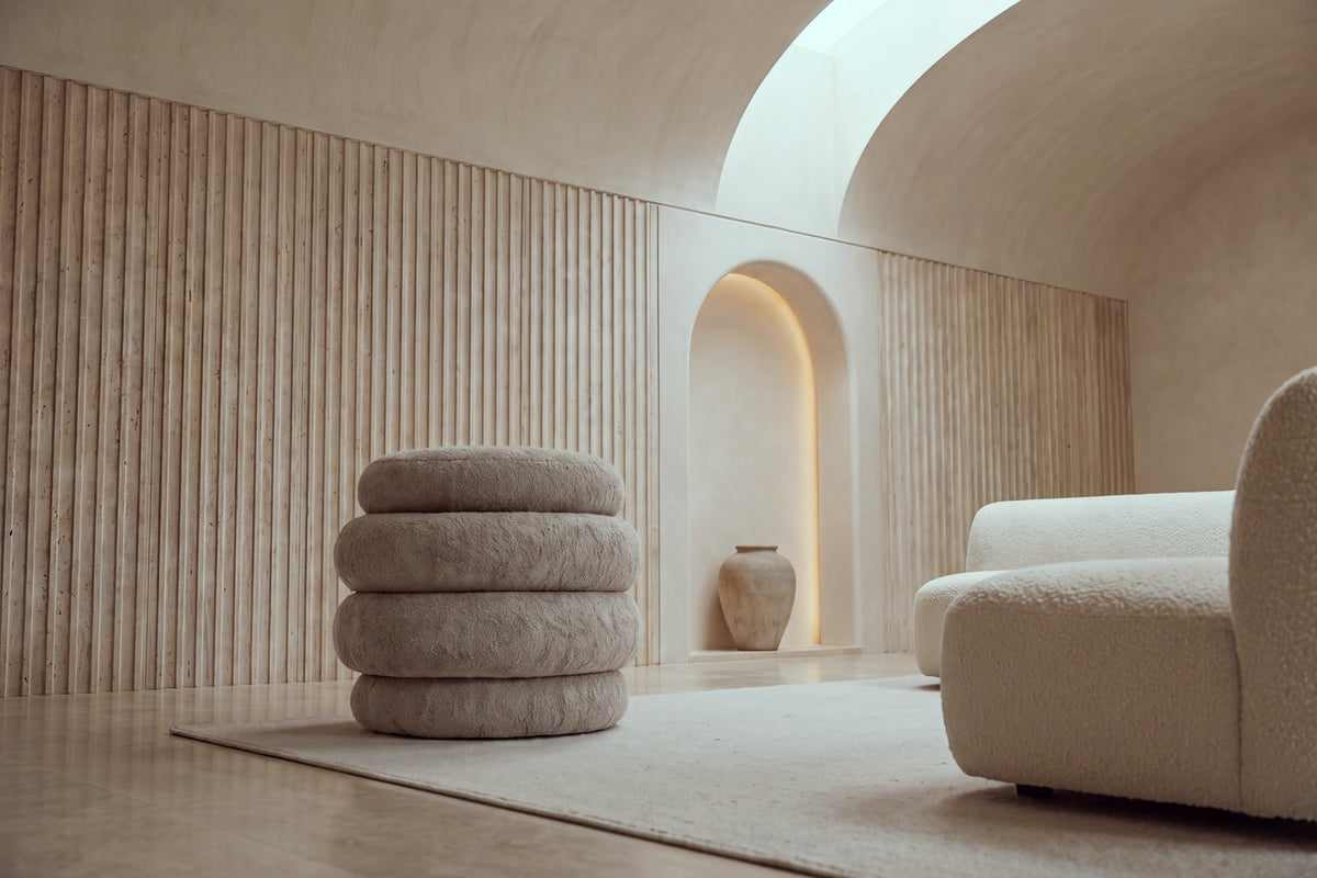 The Cisternino pouffe in taupe boucle on a wool rug in a vaulted travertine room