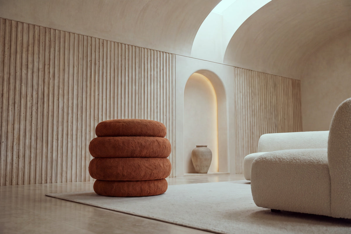 The Cisternino pouffe in terracotta boucle on a wool rug in a vaulted travertine room