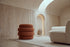 The Cisternino pouffe in terracotta boucle on a wool rug in a vaulted travertine room