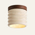 The Costa travertine flush ceiling light, a ribbed cream stone cylinder with a dark wood cap, lit from below
