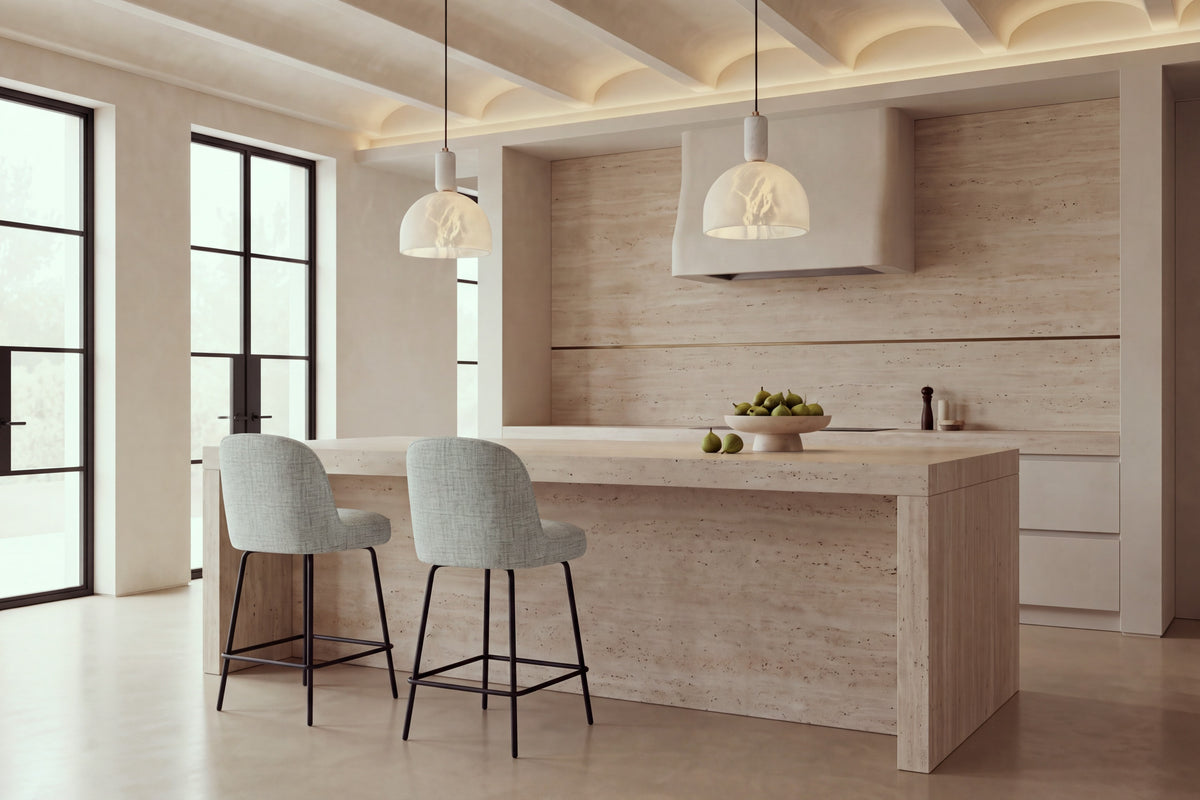 Two Deiva Counter Stools in light grey at a travertine kitchen island beneath alabaster pendants