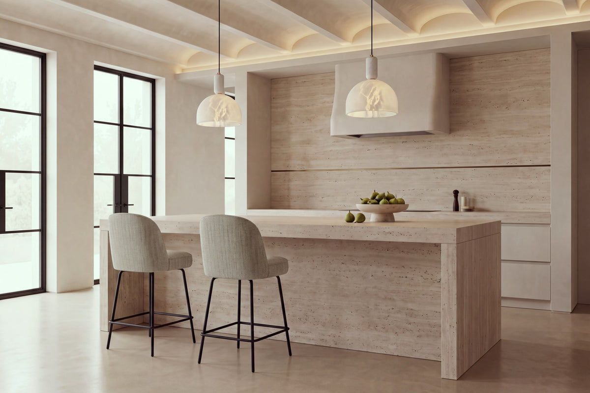 Two Deiva Counter Stools in taupe at a travertine kitchen island beneath alabaster pendants