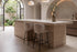Two Framura Counter Stools in beige at a travertine kitchen island under a vaulted plaster ceiling