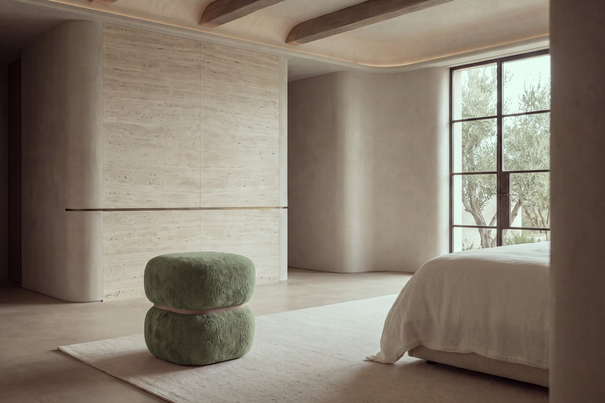 The Gallipoli pouffe in green boucle at the foot of a bed in a calm travertine bedroom