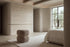 The Gallipoli pouffe in taupe boucle at the foot of a bed in a calm travertine bedroom