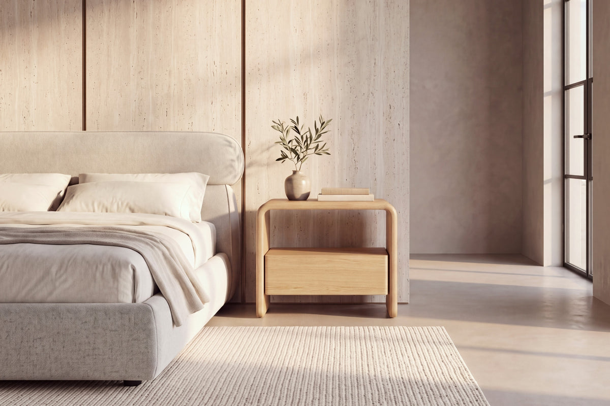 The Gargnano Bedside Table in oak beside the Positano bed against a travertine slab wall