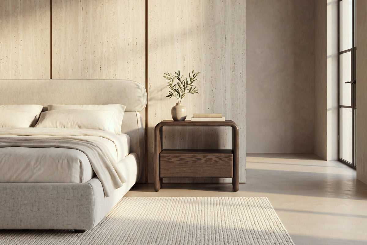 The Gargnano Bedside Table in walnut beside the Positano bed against a travertine slab wall