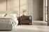The Gargnano Bedside Table in walnut beside the Positano bed against a travertine slab wall
