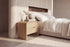 The Limone Bedside Table in oak beside the Positano bed against a fluted travertine wall