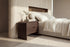 The Limone Bedside Table in walnut beside the Positano bed against a fluted travertine wall