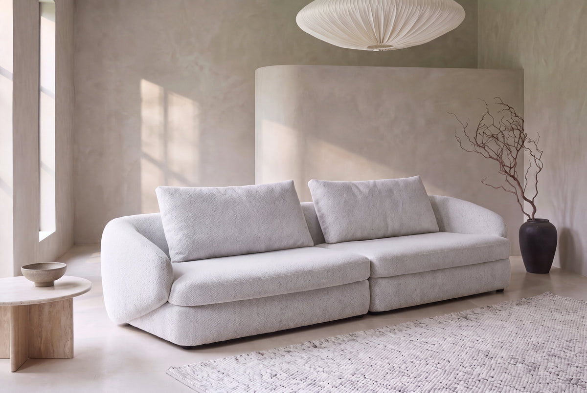 The Livorno Sofa in light grey bouclé in a soft stone-grey plaster living room with sunlight and a paper pendant