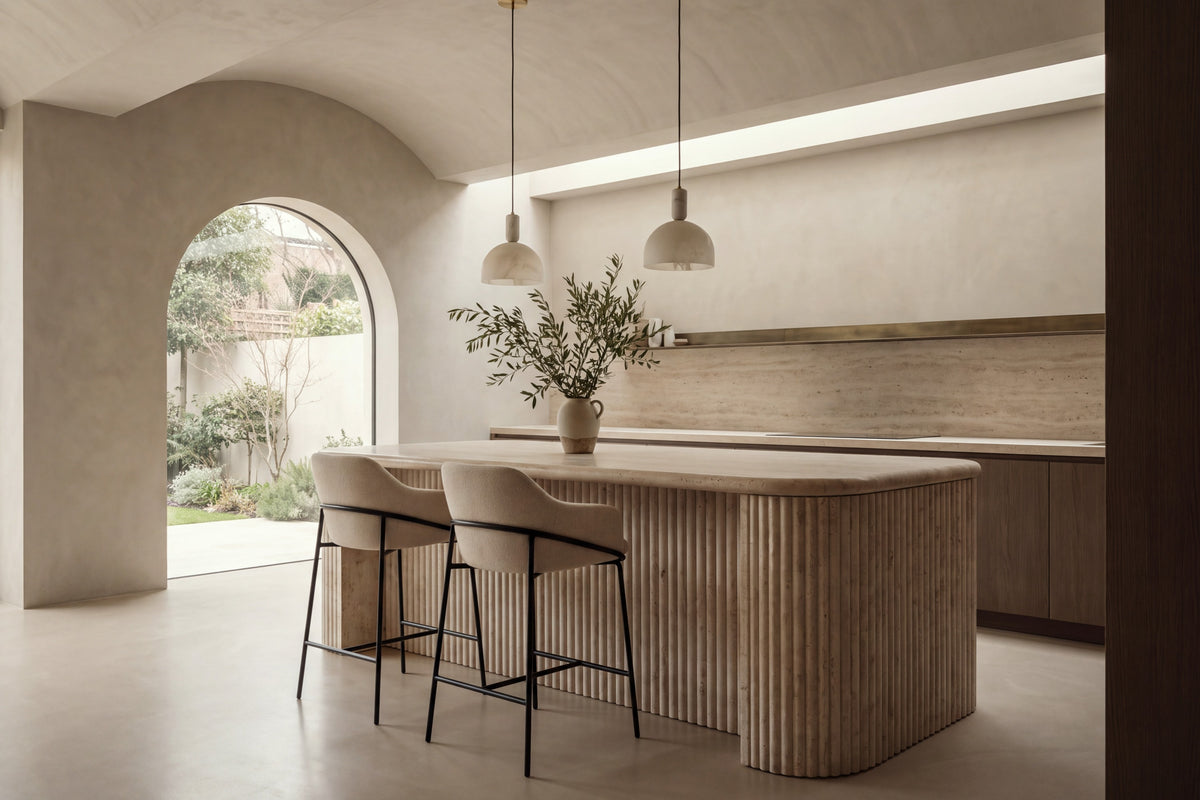 Two Moneglia Counter Stools in beige with black legs at a fluted travertine kitchen island beneath alabaster pendants
