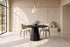 The Monza Round Dining Table in black with Norcia chairs beneath a Cupola alabaster pendant against a travertine slab wall
