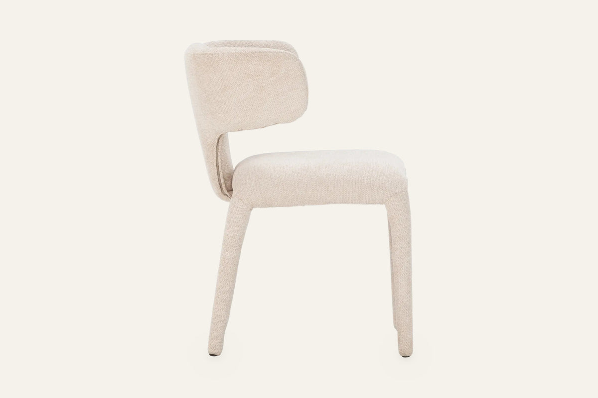 The Nemi Dining Chair in beige, fully upholstered curved dining chair, studio view