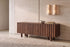 The Noli Fluted TV Unit in walnut against a travertine wall beneath a pair of alabaster wall lights