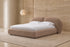The Noto Bed in soft clay boucle with a double-arched headboard in a travertine bedroom
