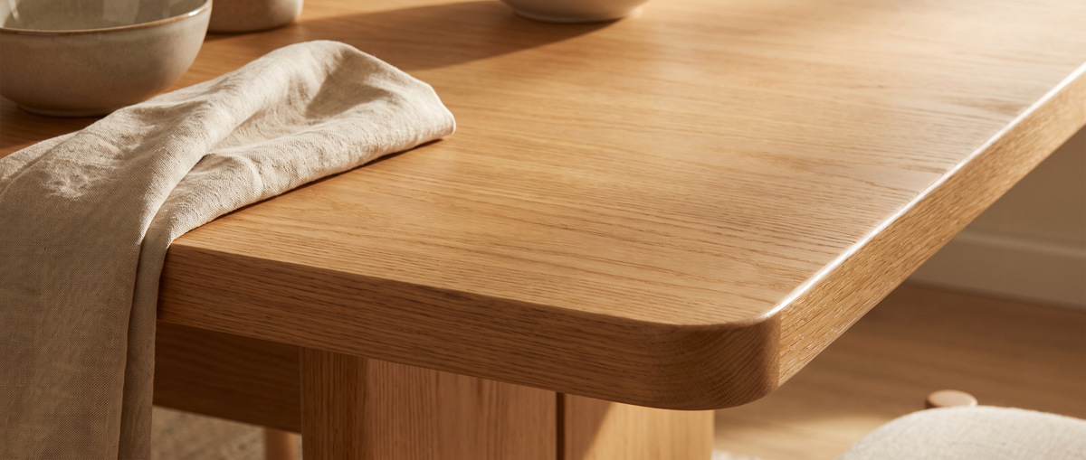 Close-up of a warm oak dining table edge with a linen napkin