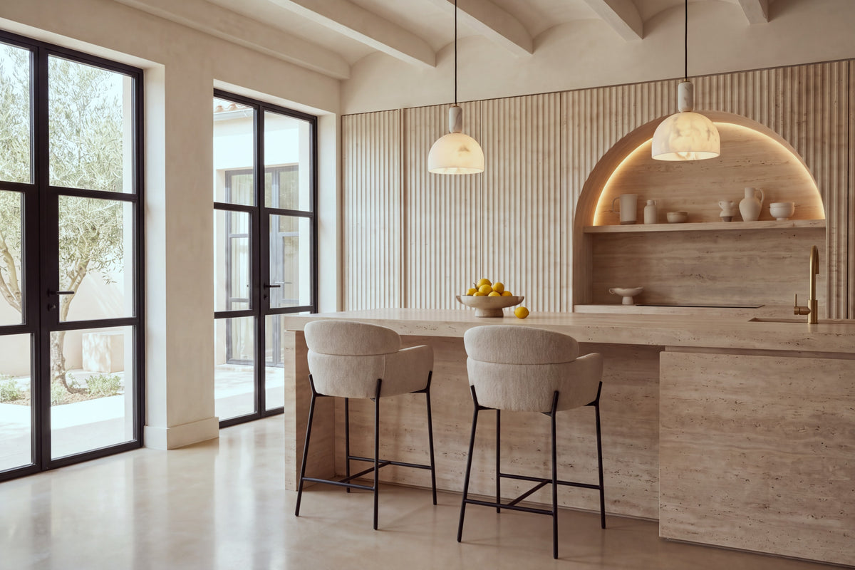 Two Recco Counter Stools in beige at a travertine kitchen island beneath alabaster pendants
