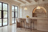 Two Recco Counter Stools in beige at a travertine kitchen island beneath alabaster pendants