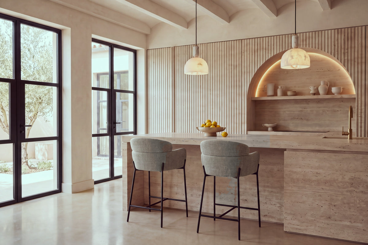 Two Recco Counter Stools in taupe at a travertine kitchen island beneath alabaster pendants