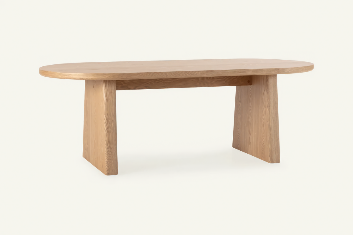 The Sutri Oval Dining Table in natural, oval dining table on panel legs, studio view
