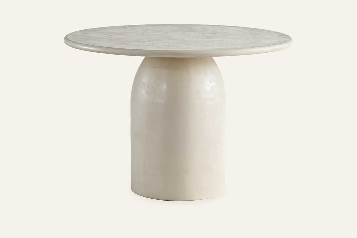 The Tellaro Round Dining Table in cream, cream cement-effect round dining table on a bell pedestal, studio view