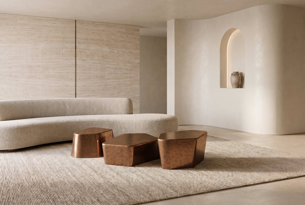 The Stromboli Coffee Table Set in bronze in a living room with a travertine wall, curved plaster and a boucle sofa