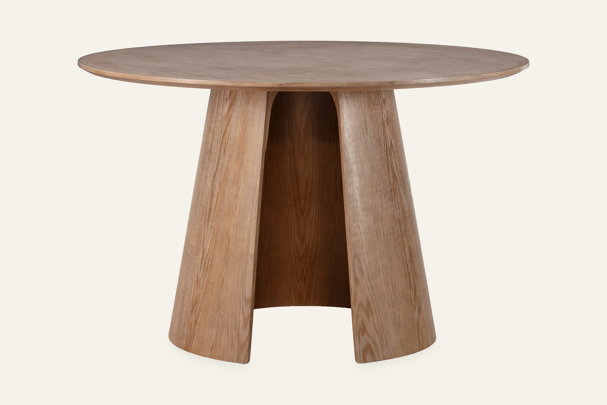 The Tropea Round Dining Table in washed oak, round dining table on a curved panel pedestal, studio view