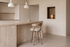 The Novara Swivel Bar Stool in beige and washed oak at a fluted travertine kitchen island beneath Cupola alabaster pendants