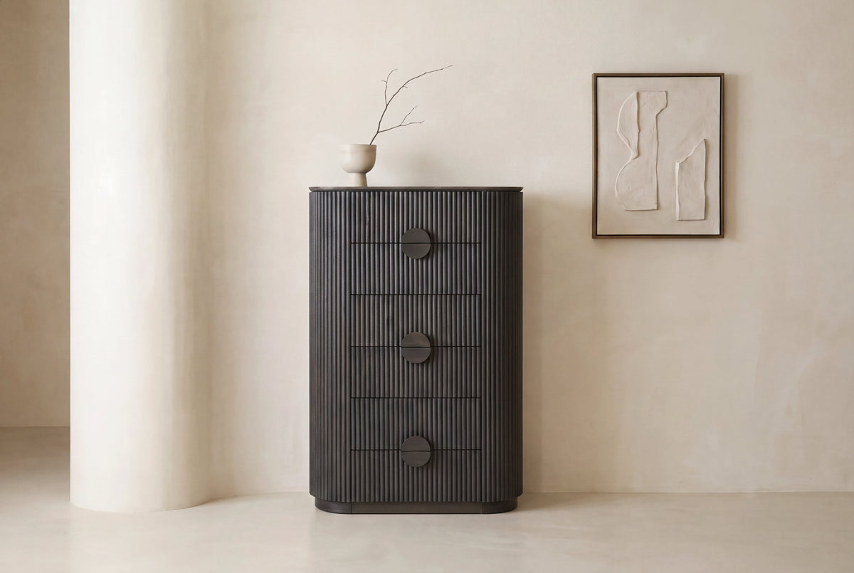 The Bevagna Fluted Marble Tallboy in dark ash against a pale plaster wall