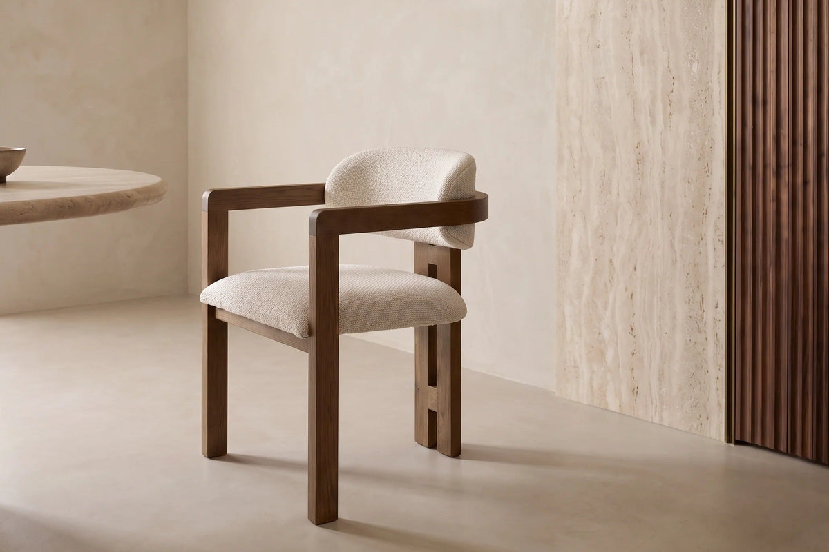 The Gubbio Dining Armchair beside a travertine dining table