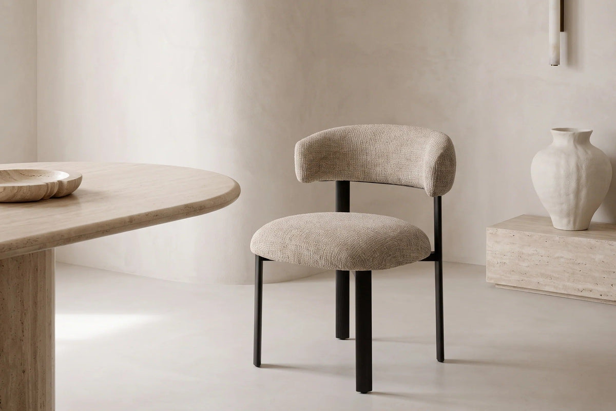 The Narni Dining Chair beside an oval travertine dining table