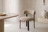 The Narni Dining Chair beside an oval travertine dining table